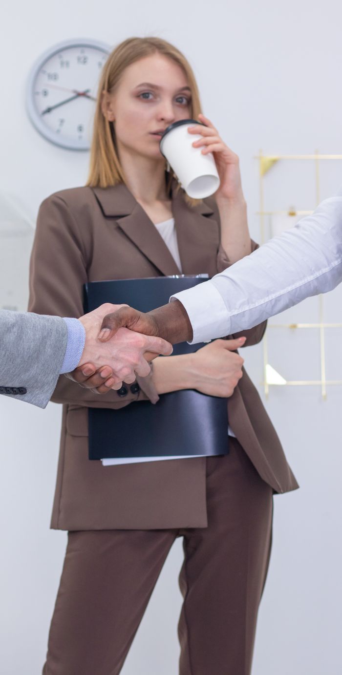 A businesswoman witnesses a professional handshake in a modern office setting.